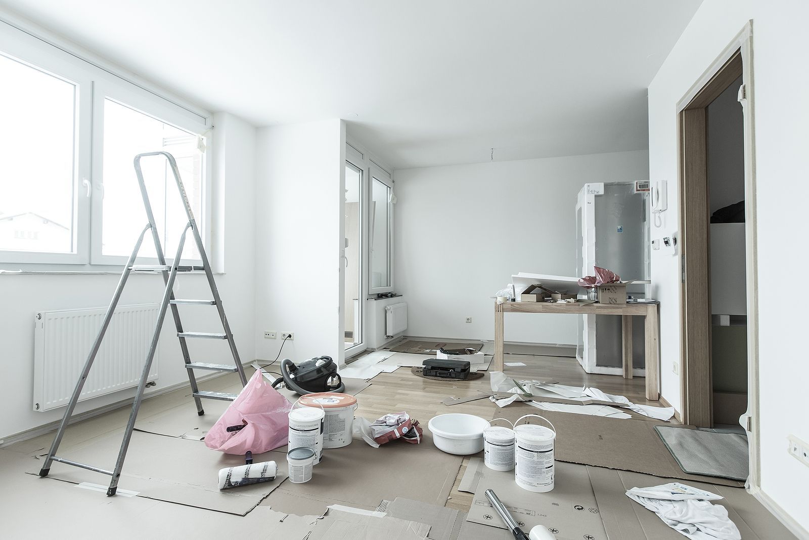 An empty room with a ladder and paint buckets on the floor.