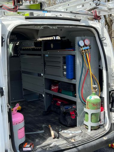 Interior view of a work van equipped with shelving units, storage bins, tools, refrigerant hoses, and gas cylinders.