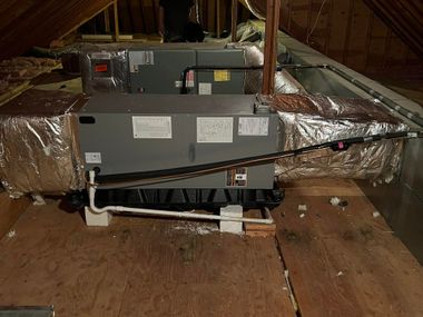 Two gray HVAC air handler units installed on elevated platforms in an unfinished attic with insulated ductwork.