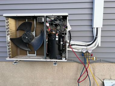 An HVAC technician’s manifold gauge set is attached to a residential outdoor heat pump unit with its side panel removed.