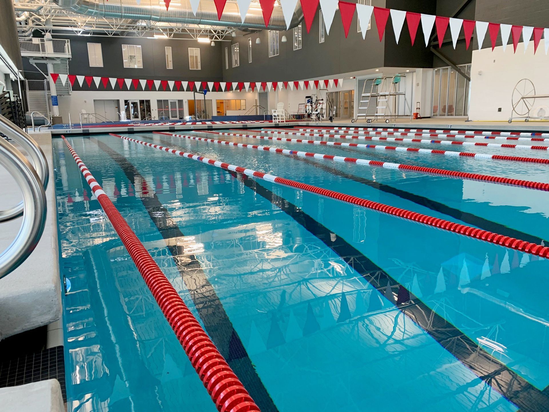 Indoor swimming pool with lane markers, red and white flags, and equipment.