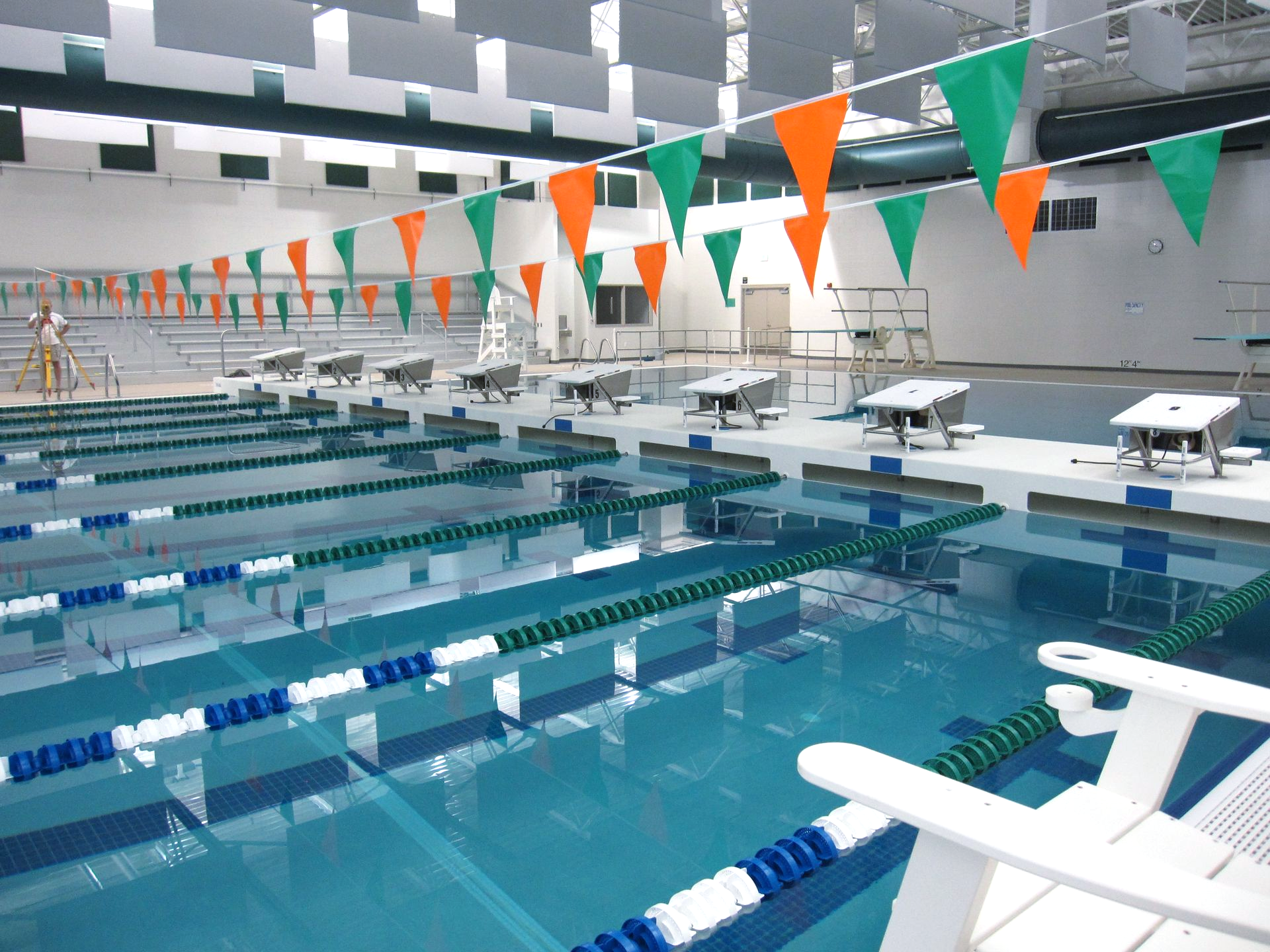 Indoor swimming pool with lane lines, starting blocks, and orange/green pennant flags.