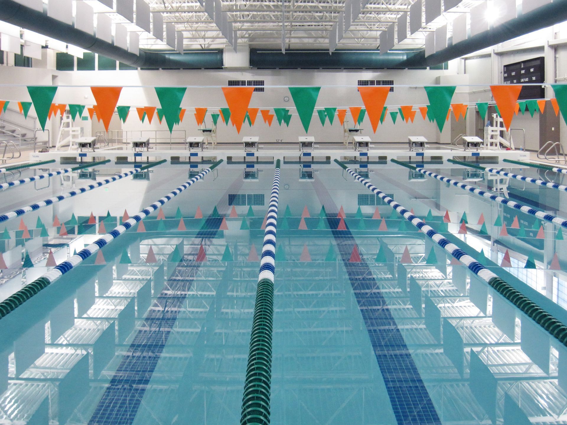 Indoor swimming pool with lanes marked by blue and white lines. Orange and green pennant banners hang overhead.
