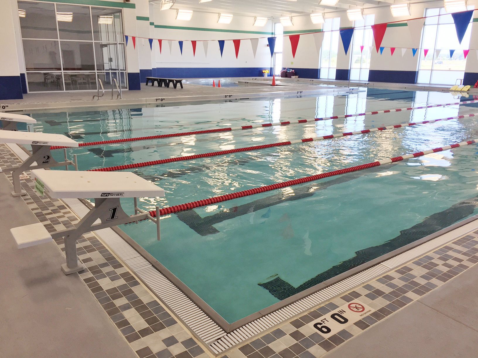 Indoor swimming pool with lane markers, diving boards, and colorful pennants.