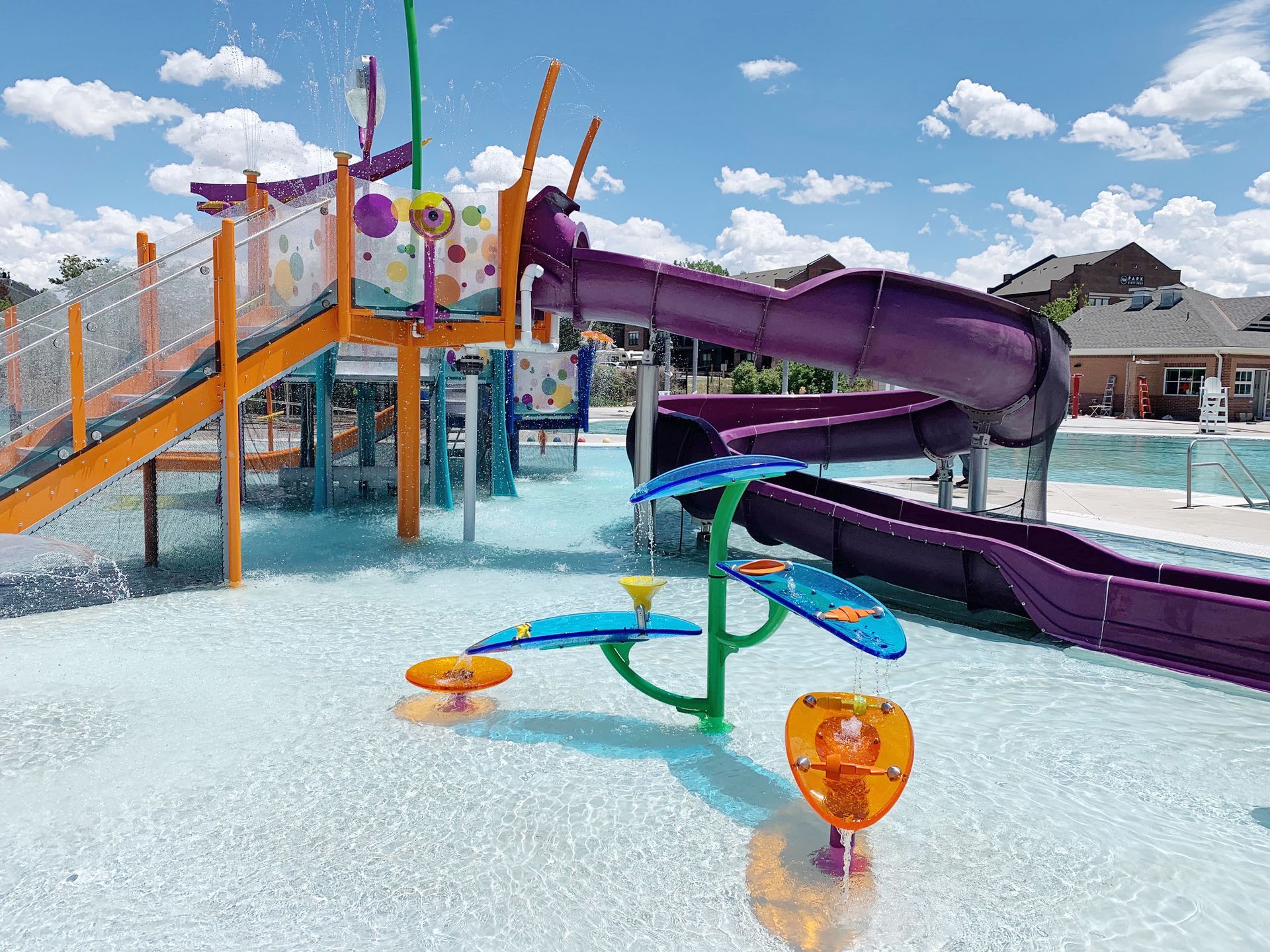 Water park with purple slide, spray features, and shallow pool under a blue sky.