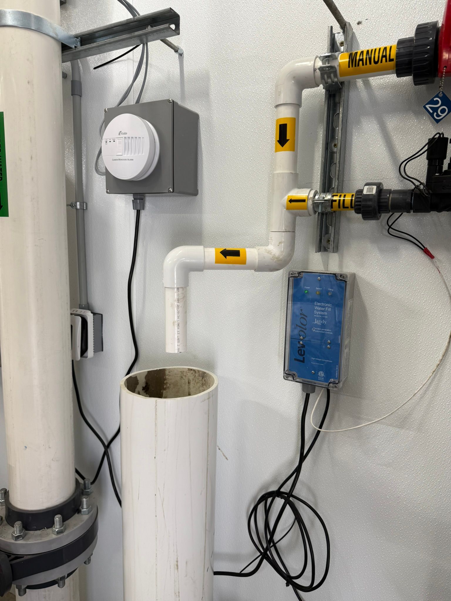 White PVC pipes and equipment against a wall, including a sensor box, chemical injectors, and a cylinder.
