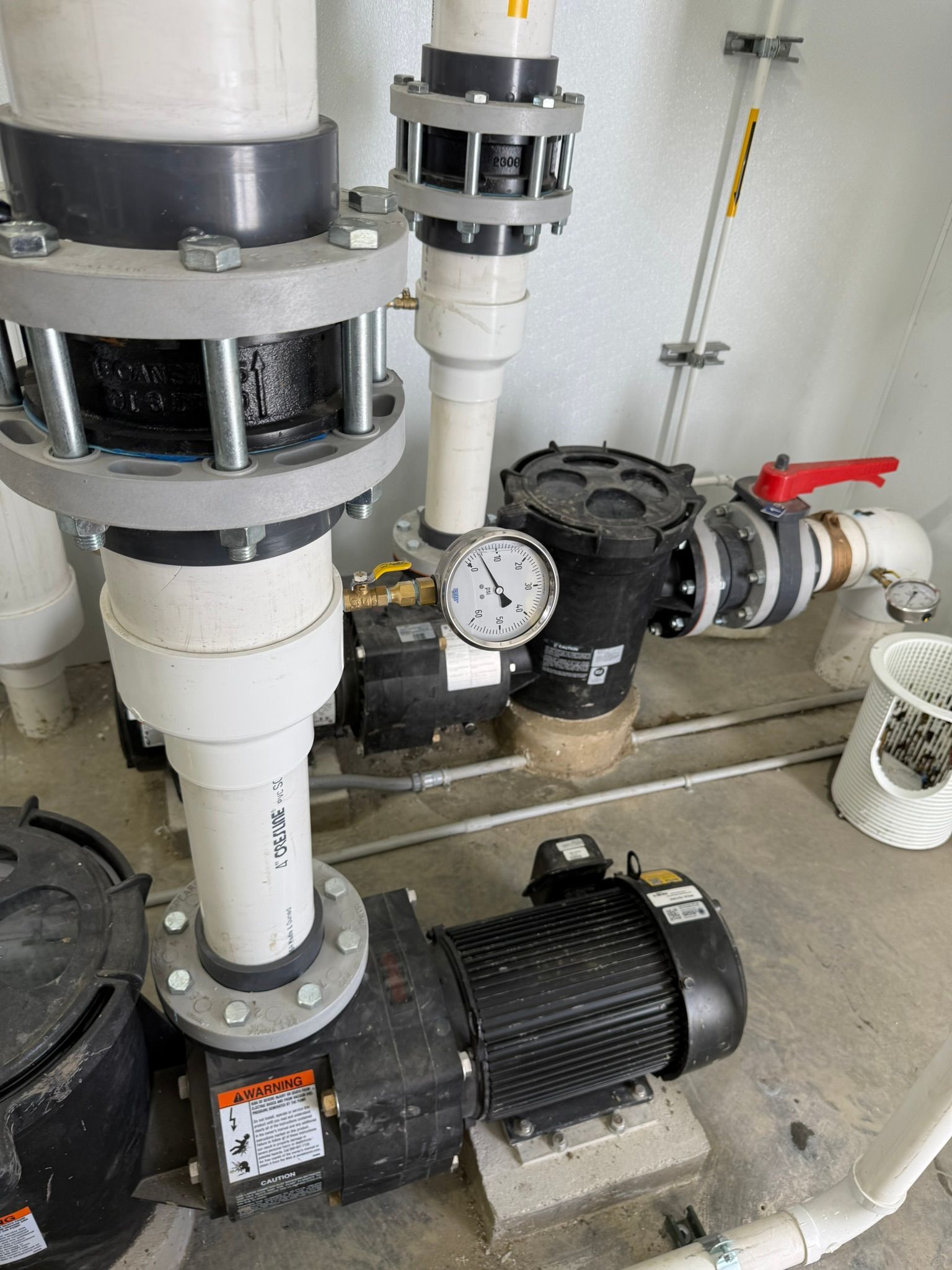 Pool equipment with two black pumps, white pipes, and a pressure gauge.