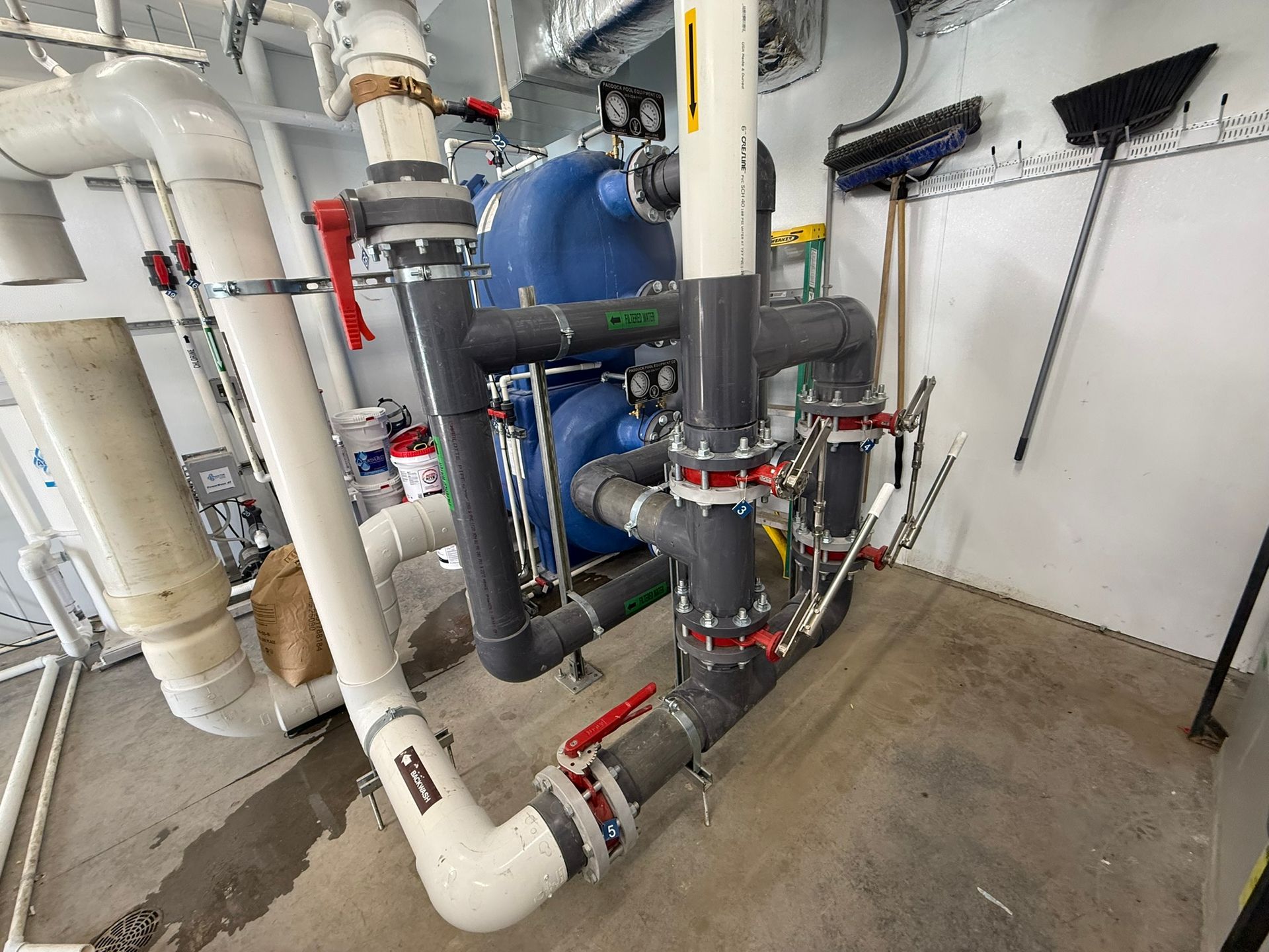 Pool equipment room with blue filter, gray pipes, and red valves.
