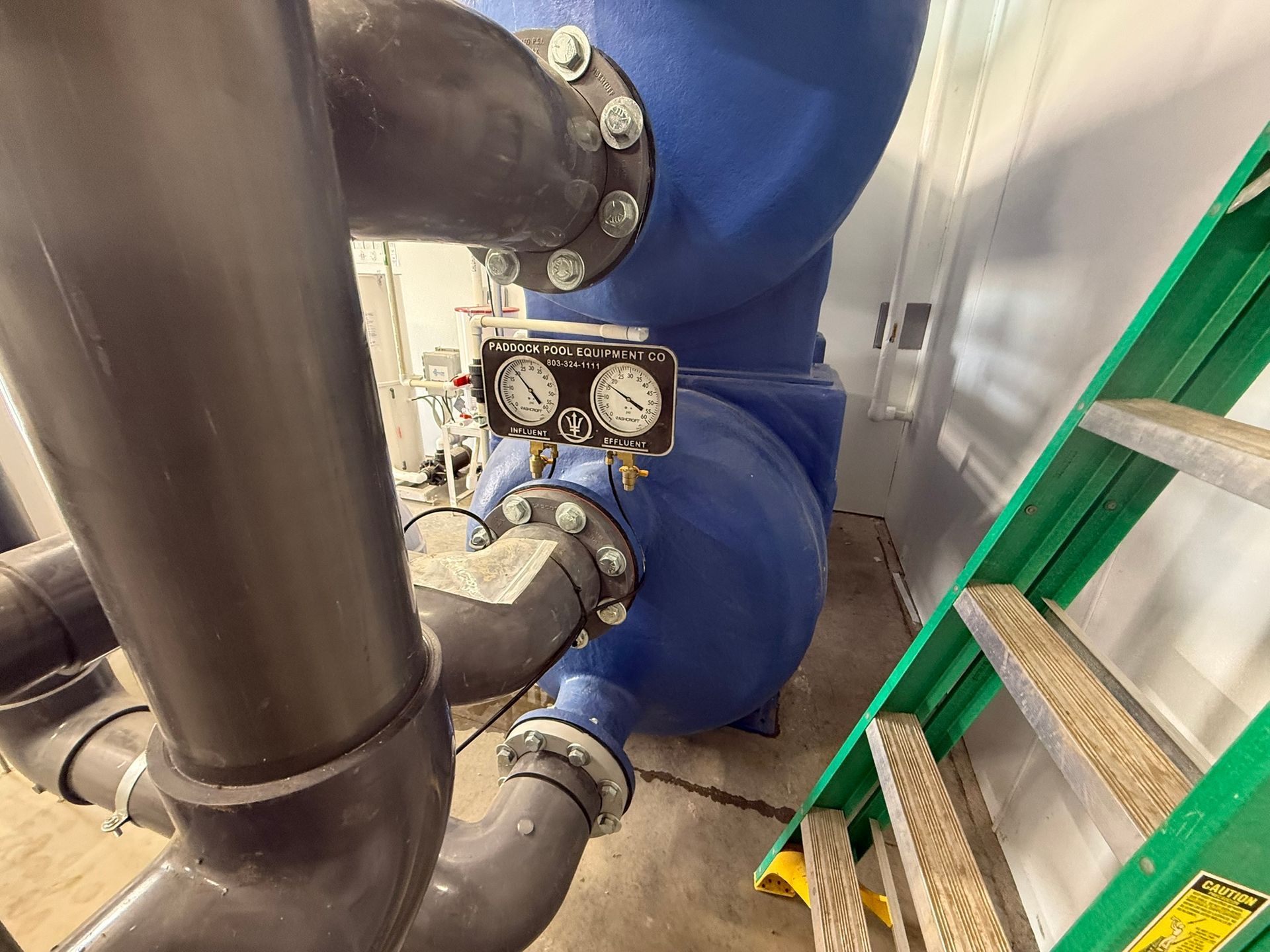 Blue water filter with pipes, gauges, and a ladder inside a facility.
