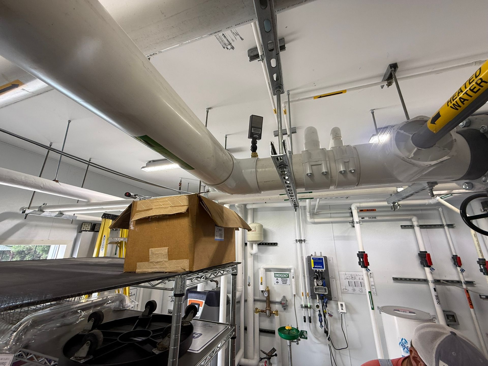 Pipes and equipment in an industrial setting with a cardboard box on a shelf.
