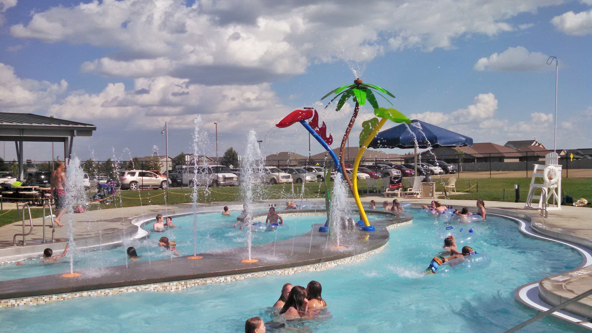 People playing in a lazy river at a water park with palm tree water features under a blue sky.