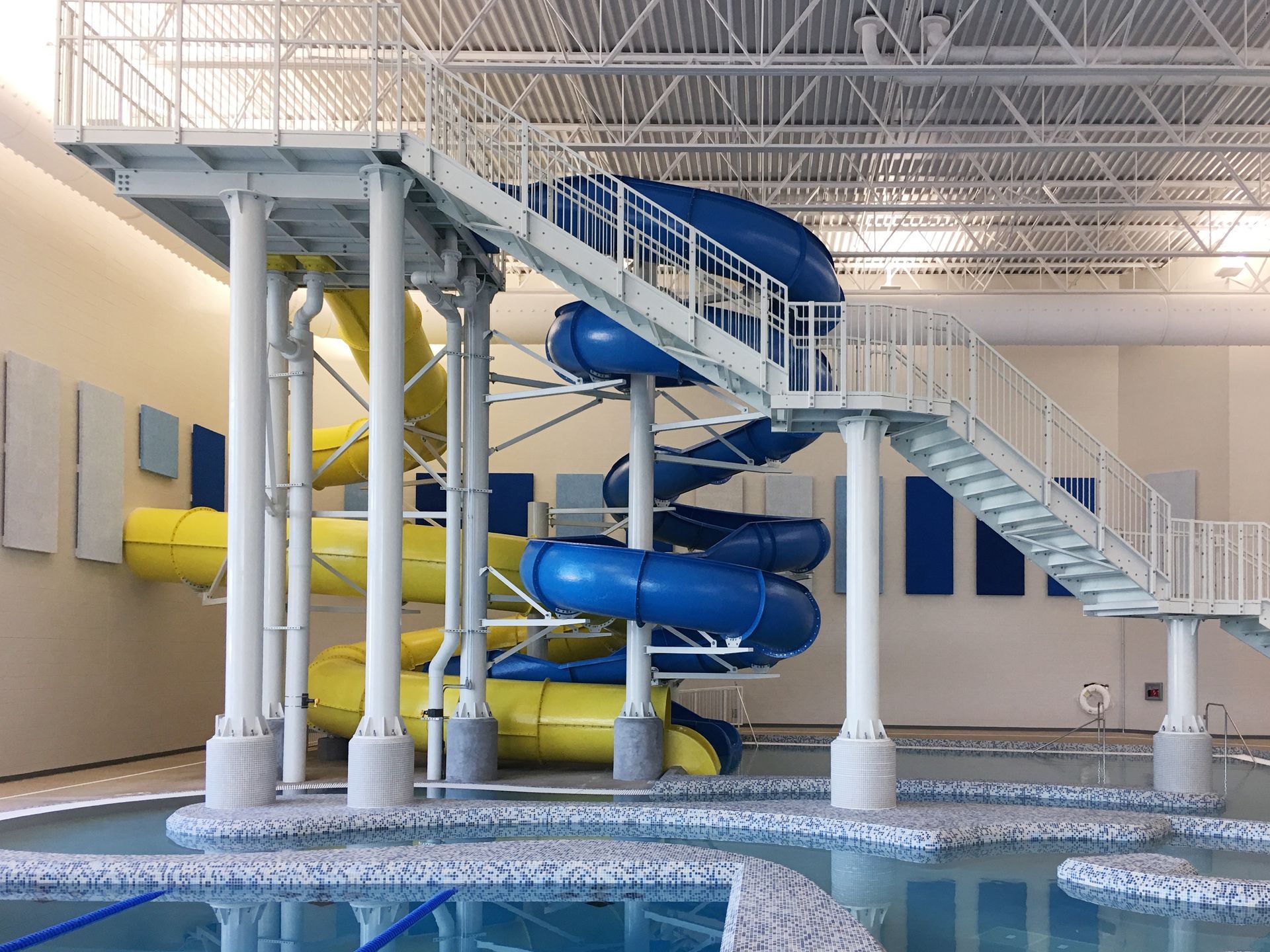 Indoor water park with blue and yellow slides, stairs, and a pool.