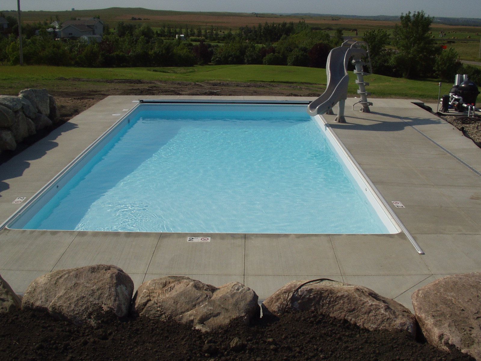 Rectangular pool with light blue water, concrete surround, and person adjusting a pool cover outdoors.
