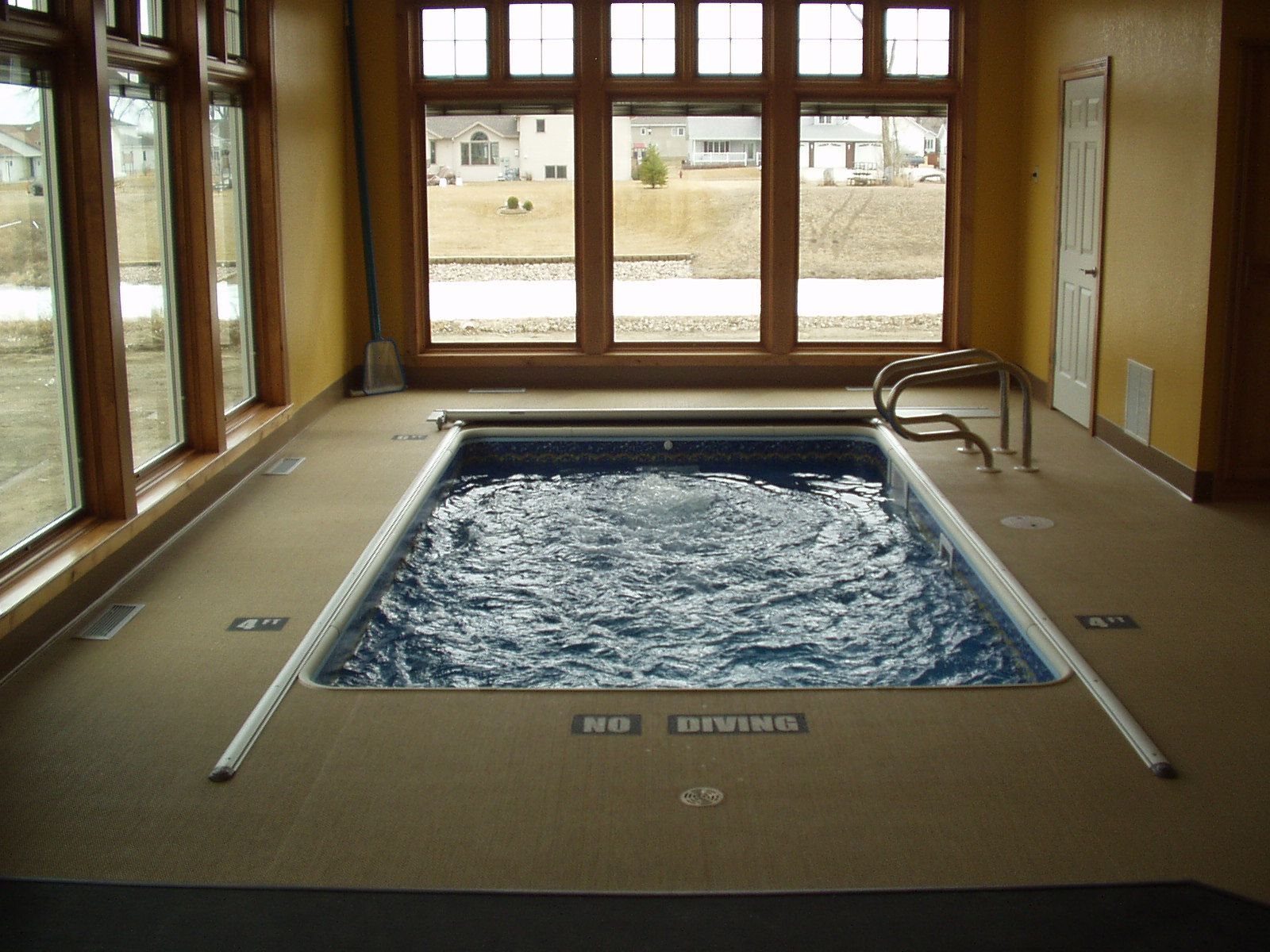 Indoor pool with jets, surrounded by windows and light-colored flooring; wooden trim and gold walls.