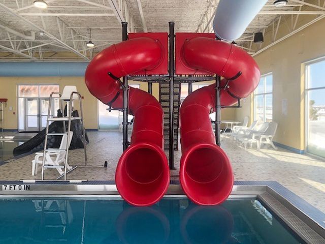 Red water slide over a swimming pool inside a building with windows.