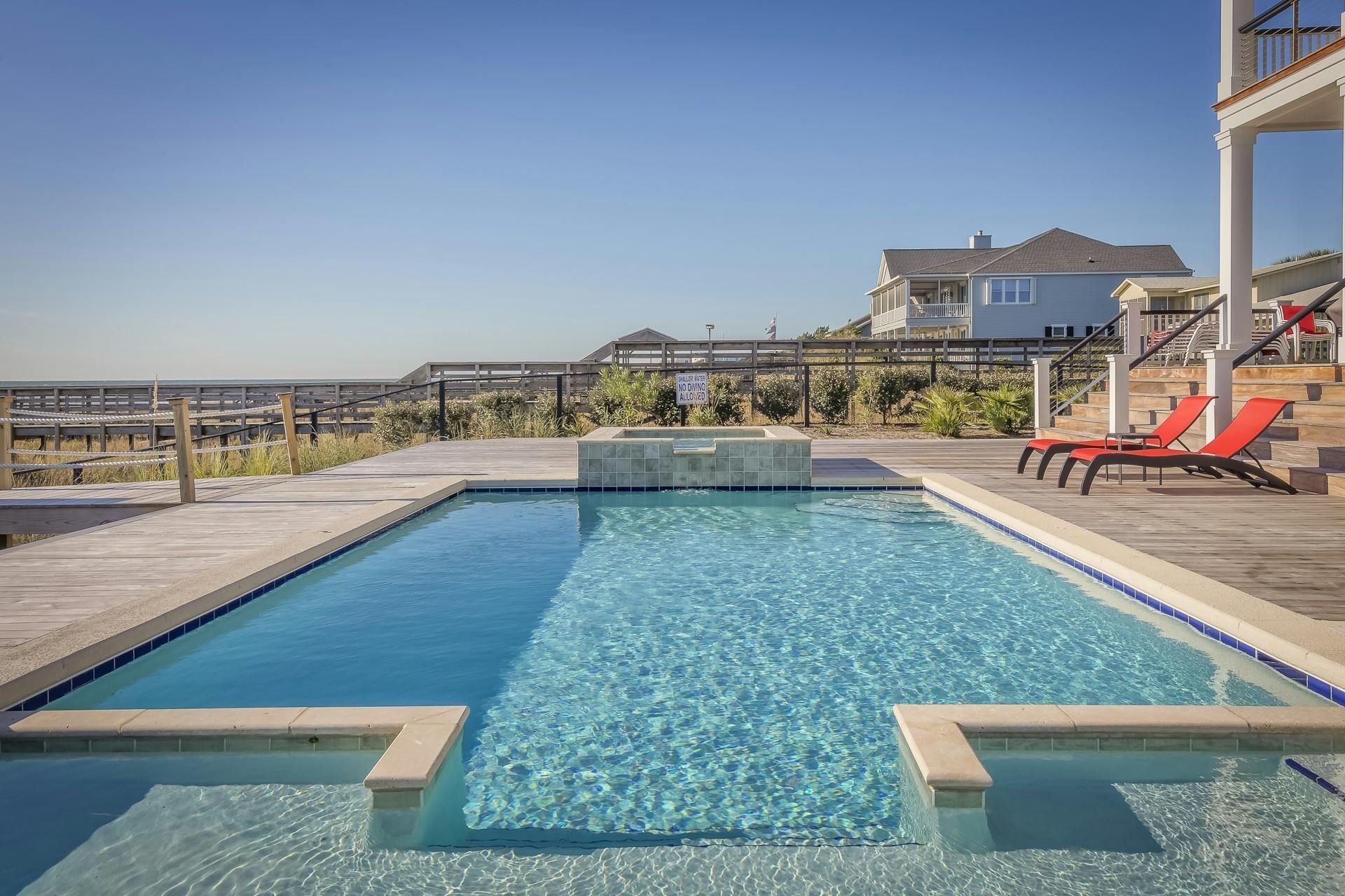 A rectangular pool with clear water, lounge chairs, and a house in the background on a sunny day.