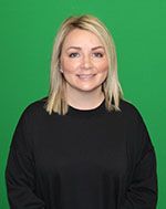 A woman in a black sweater is standing in front of a green screen.