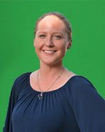 A woman in a blue shirt is smiling in front of a green screen.