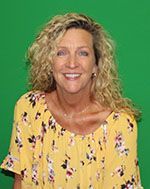 A woman in a yellow floral shirt is smiling in front of a green screen.
