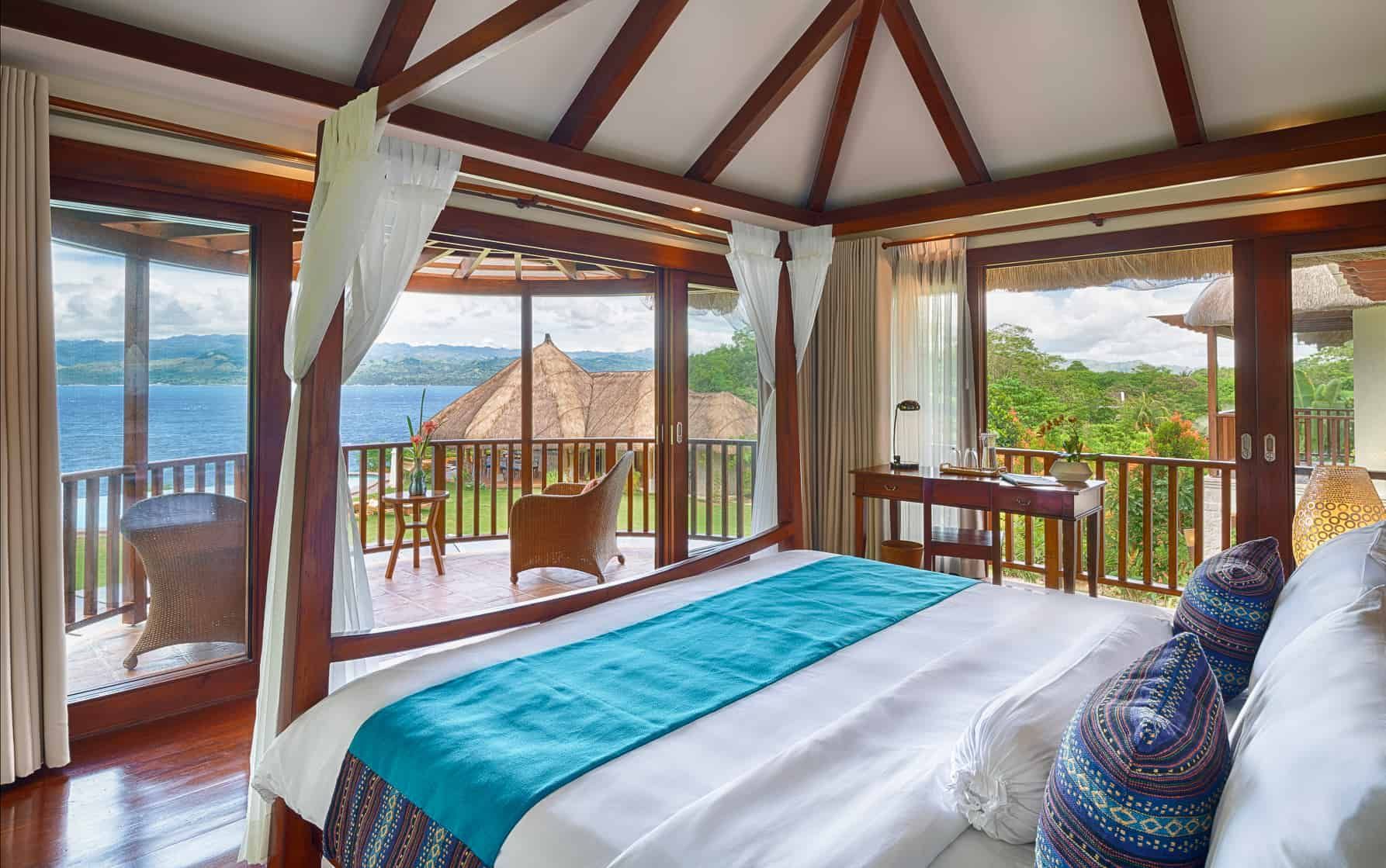 Bedroom with bed, balcony, and view of water and trees.