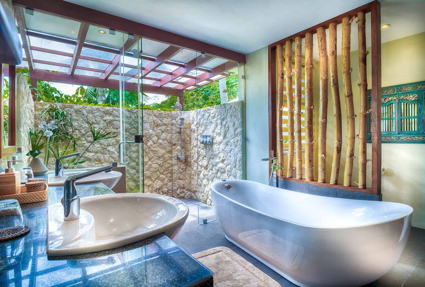Bathroom with stone wall shower, freestanding tub, wooden screen, and open-air design.