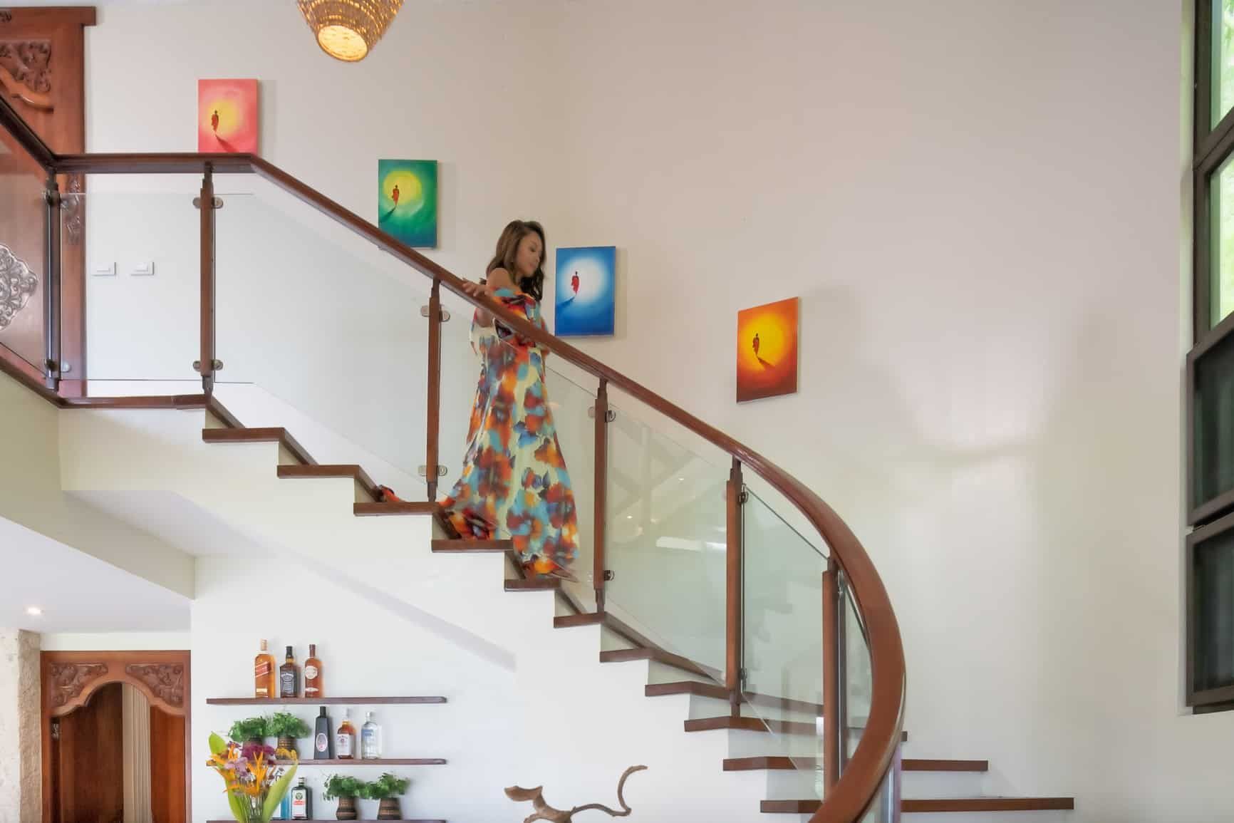 Woman descending a curved staircase in a bright, airy home; paintings on the wall.