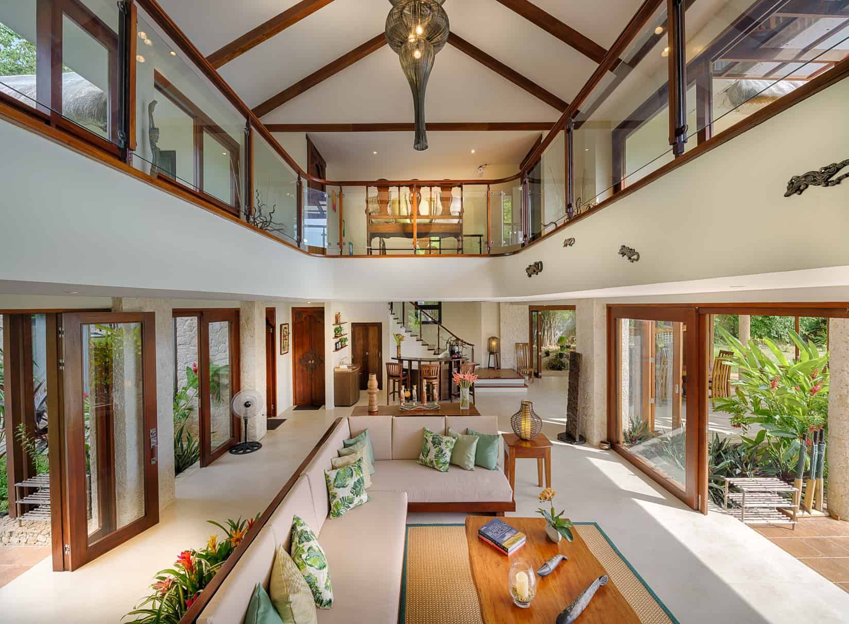 Spacious living room with high ceilings, glass balconies, and open doors to a lush garden.