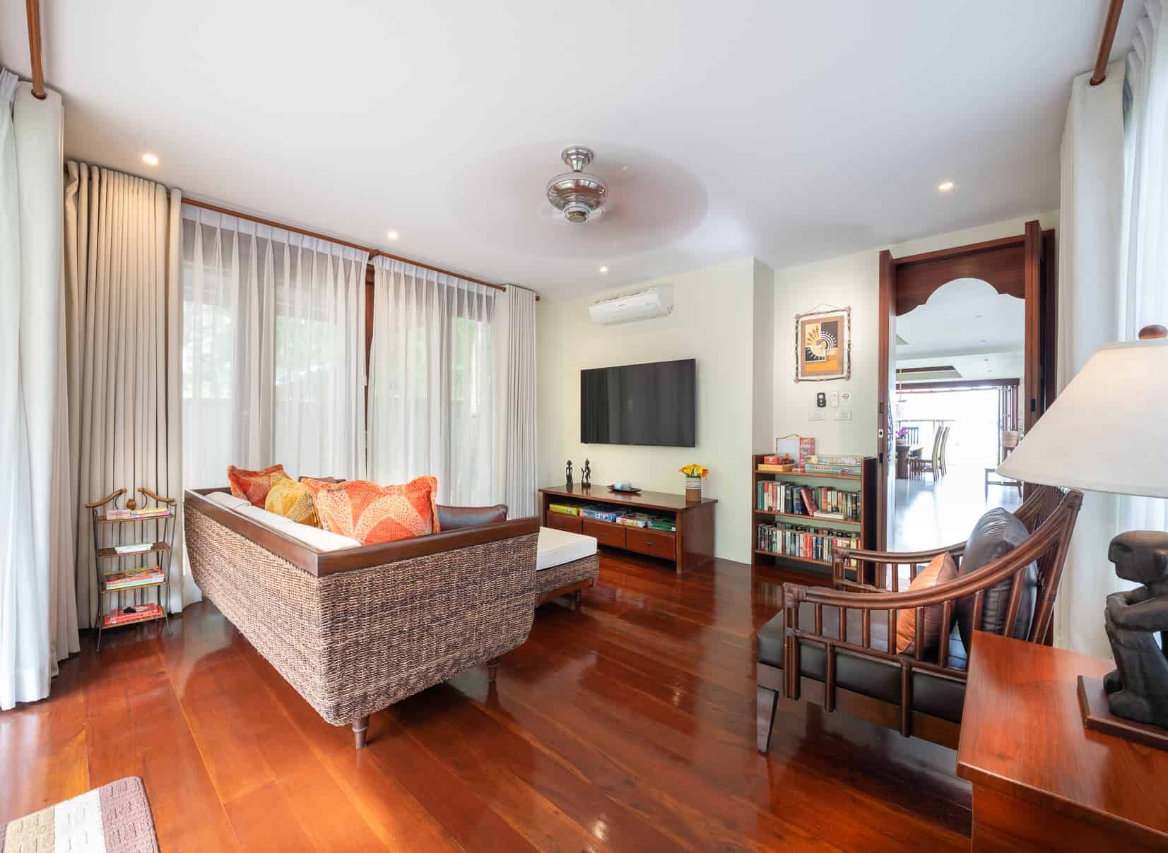Living room with wood floors, woven sofa, TV, and open doorway.
