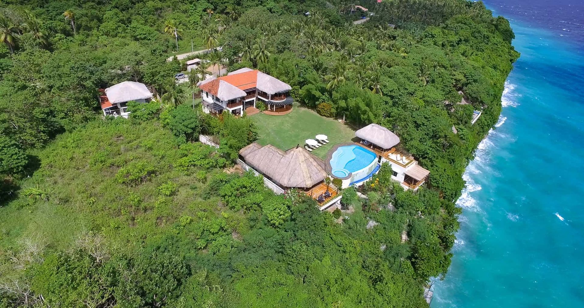 Tropical villa with ocean view, surrounded by lush green foliage and turquoise water.