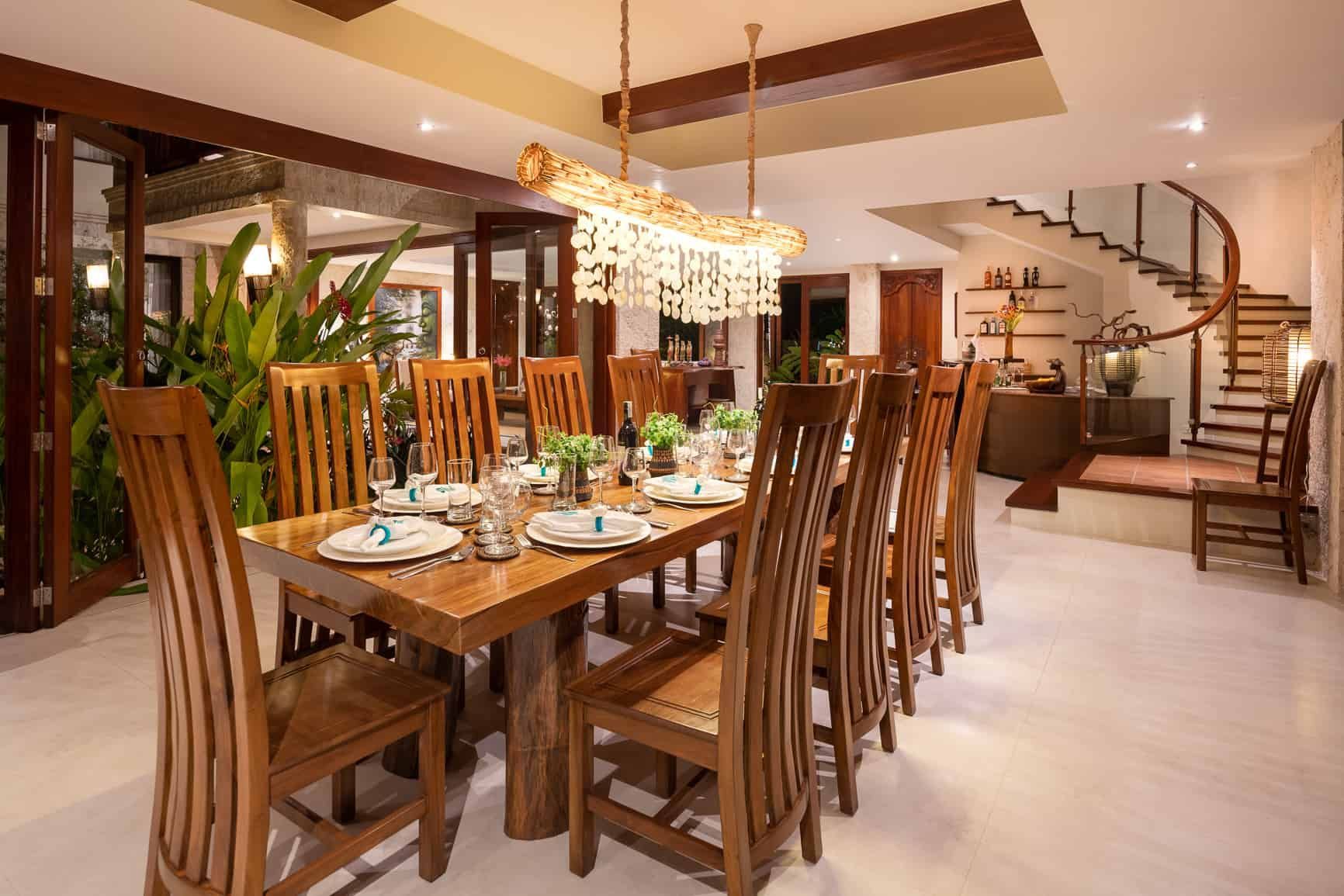 Dining room with a long wooden table set for a meal; wooden chairs, stairs, and a decorative light fixture.