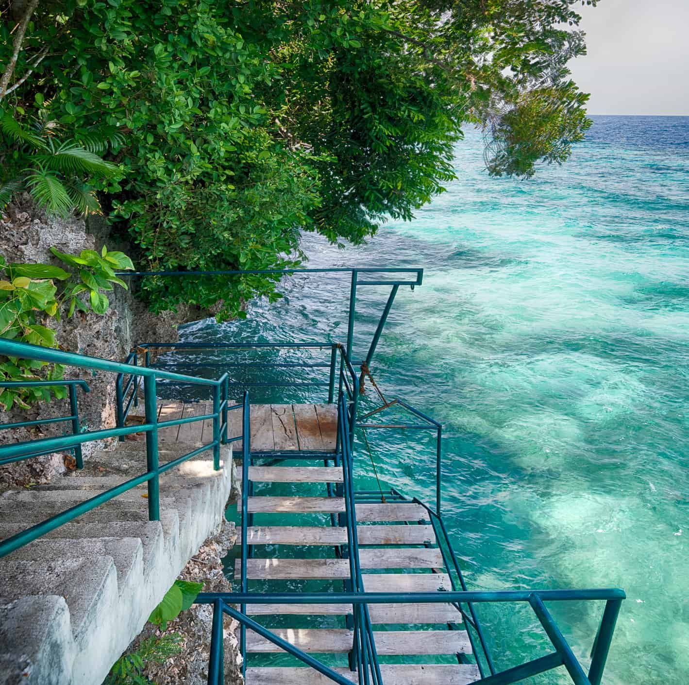 Staircase leading down to turquoise water, next to lush greenery.