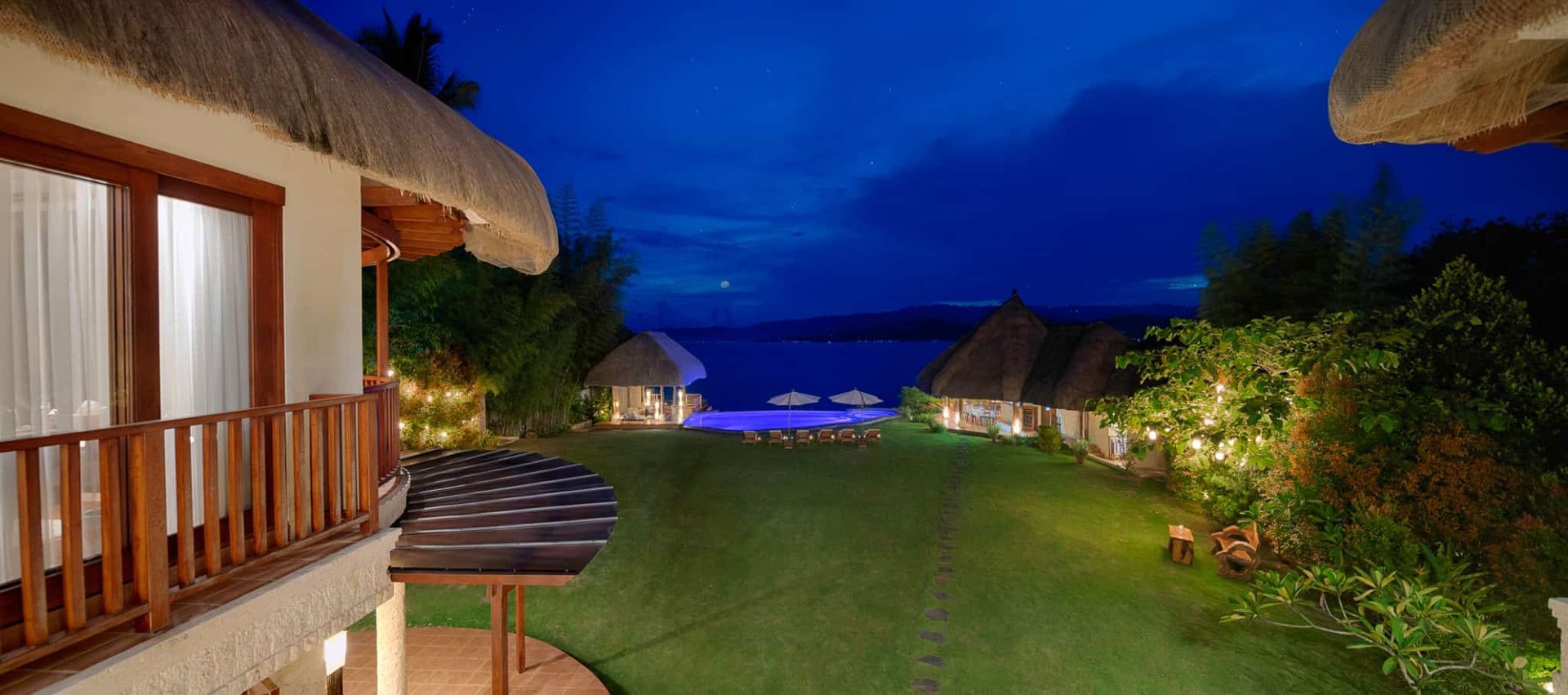 Night view of resort buildings with grass leading to the ocean. Blue sky, soft lighting.
