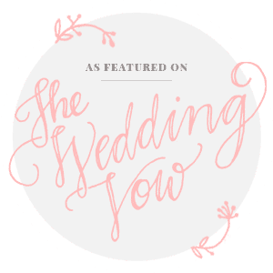 Logo for The Wedding Vow, with pink script text on a gray circle, floral accents, and