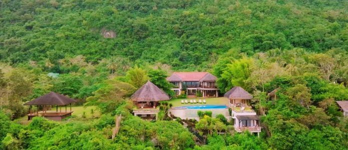 Luxury resort nestled in a lush green hillside, featuring a main house, pool, and cabanas.