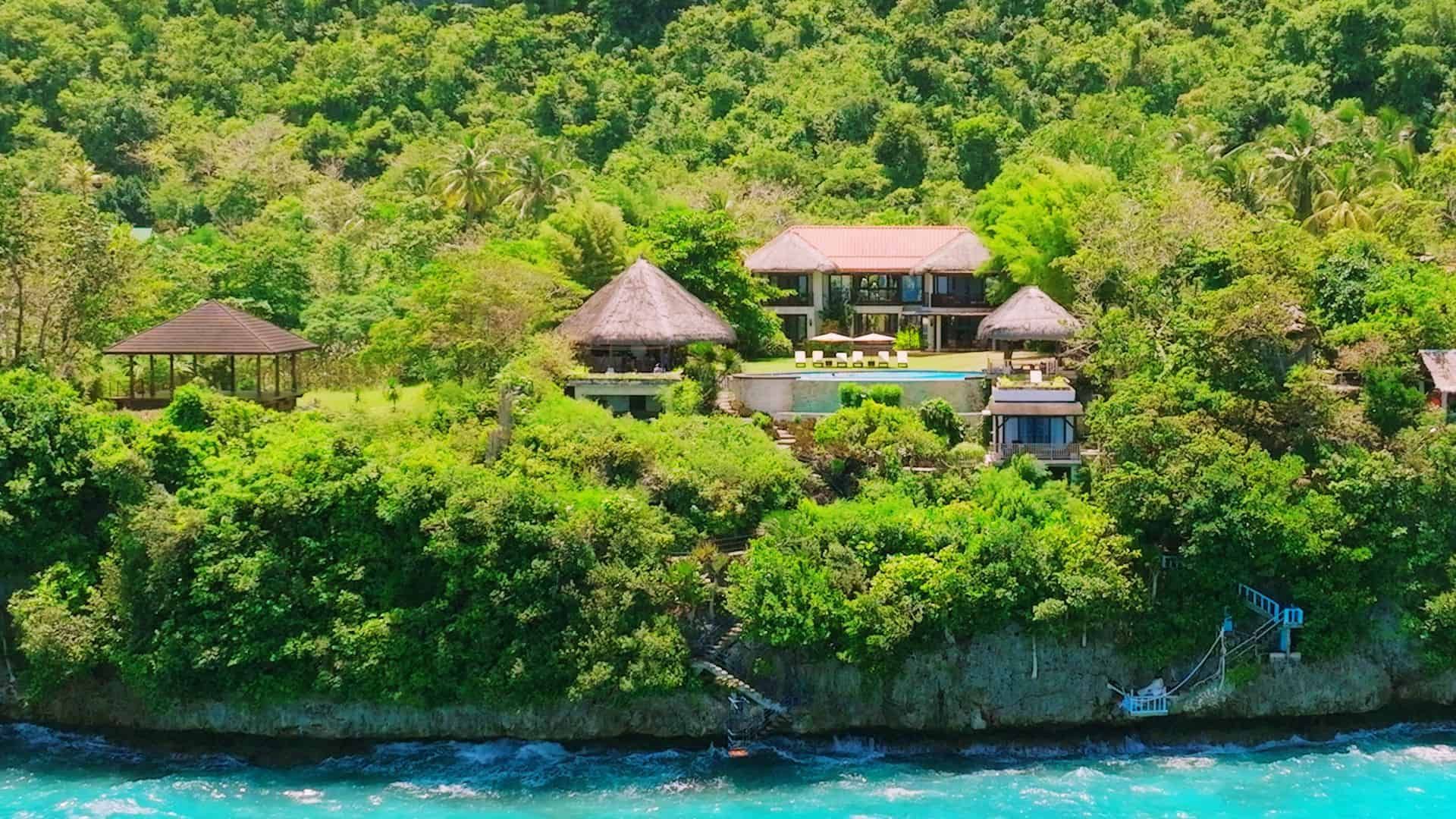 Luxurious house nestled in lush greenery, by a turquoise ocean.