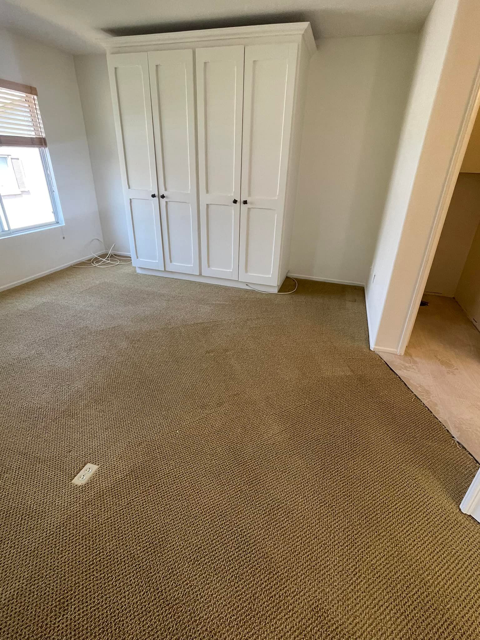 An empty room with a carpeted floor and white cabinets.