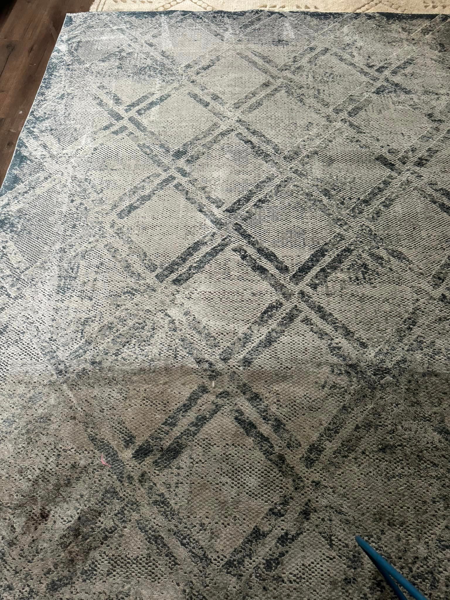 A rug is being cleaned with a vacuum cleaner on a wooden floor.