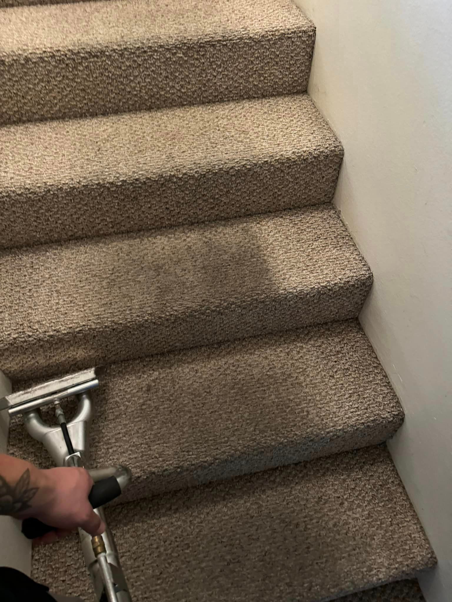 A person is cleaning a carpeted staircase with a vacuum cleaner.