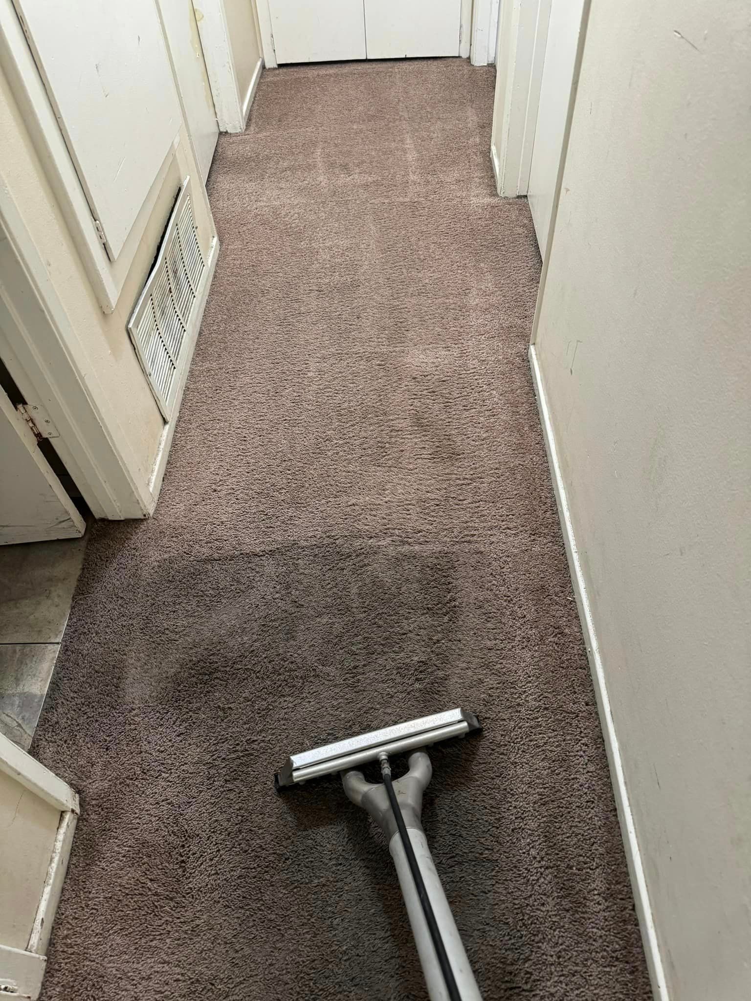 A vacuum cleaner is being used to clean a carpet in a hallway.
