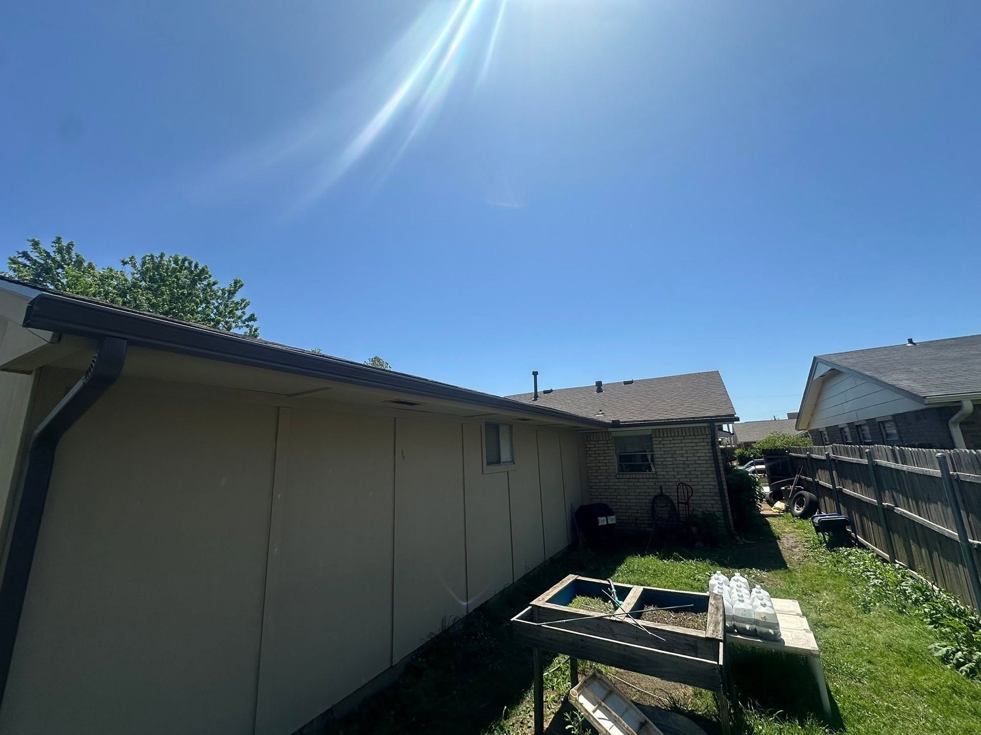Backyard beside a beige house with a picnic table, grass, and a bright sunny sky