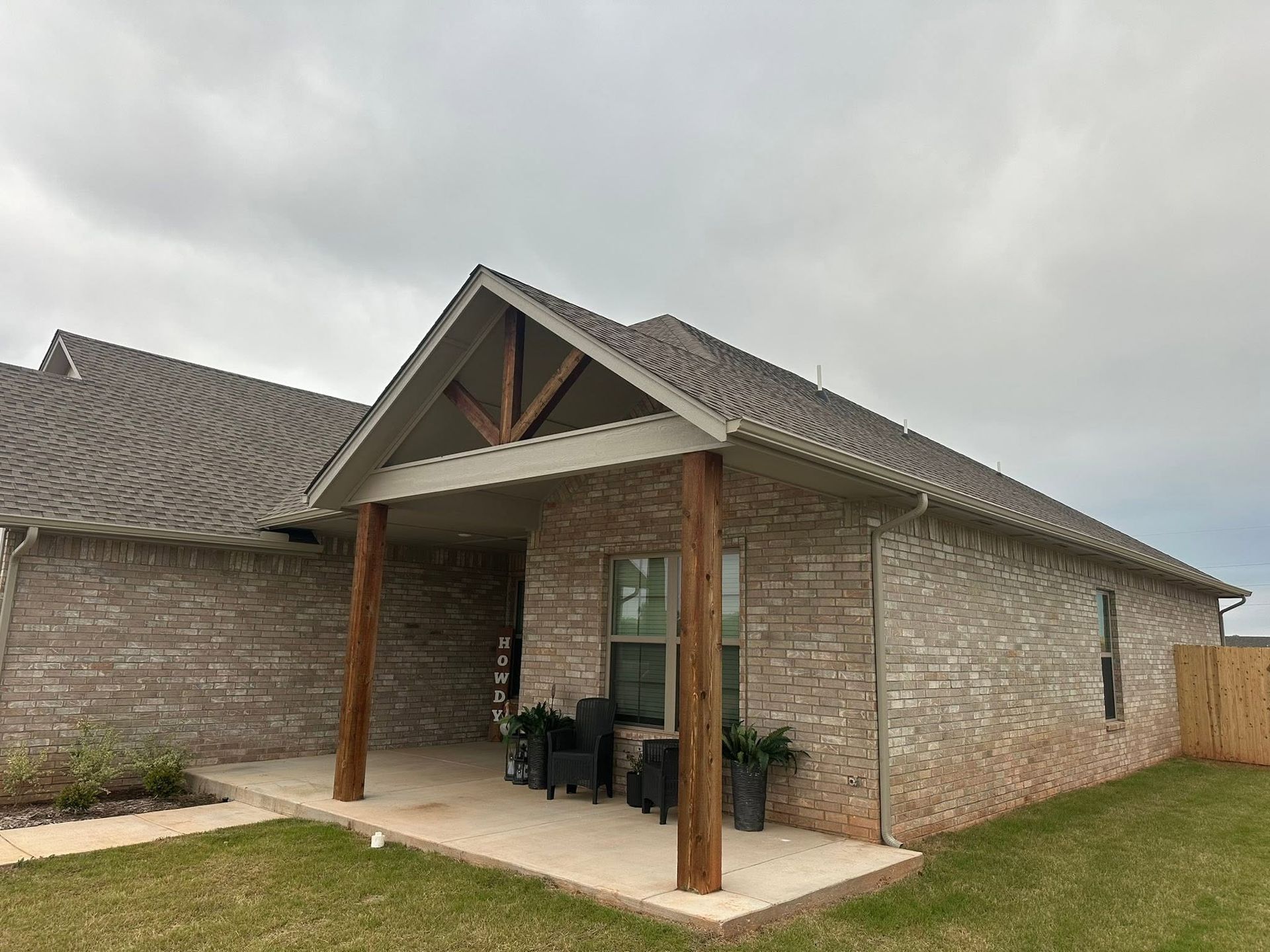 Covered front porch of a brick house with wooden posts under a cloudy sky