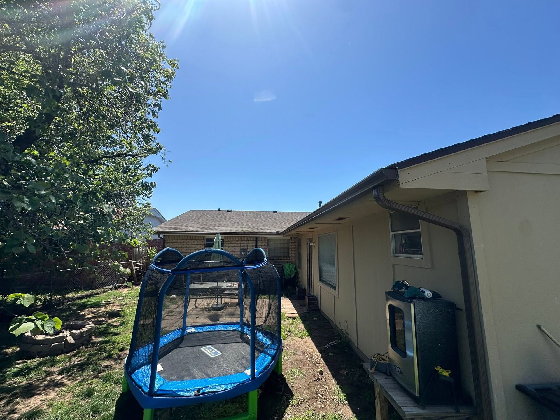 Backyard with a blue trampoline beside a house under a clear sky