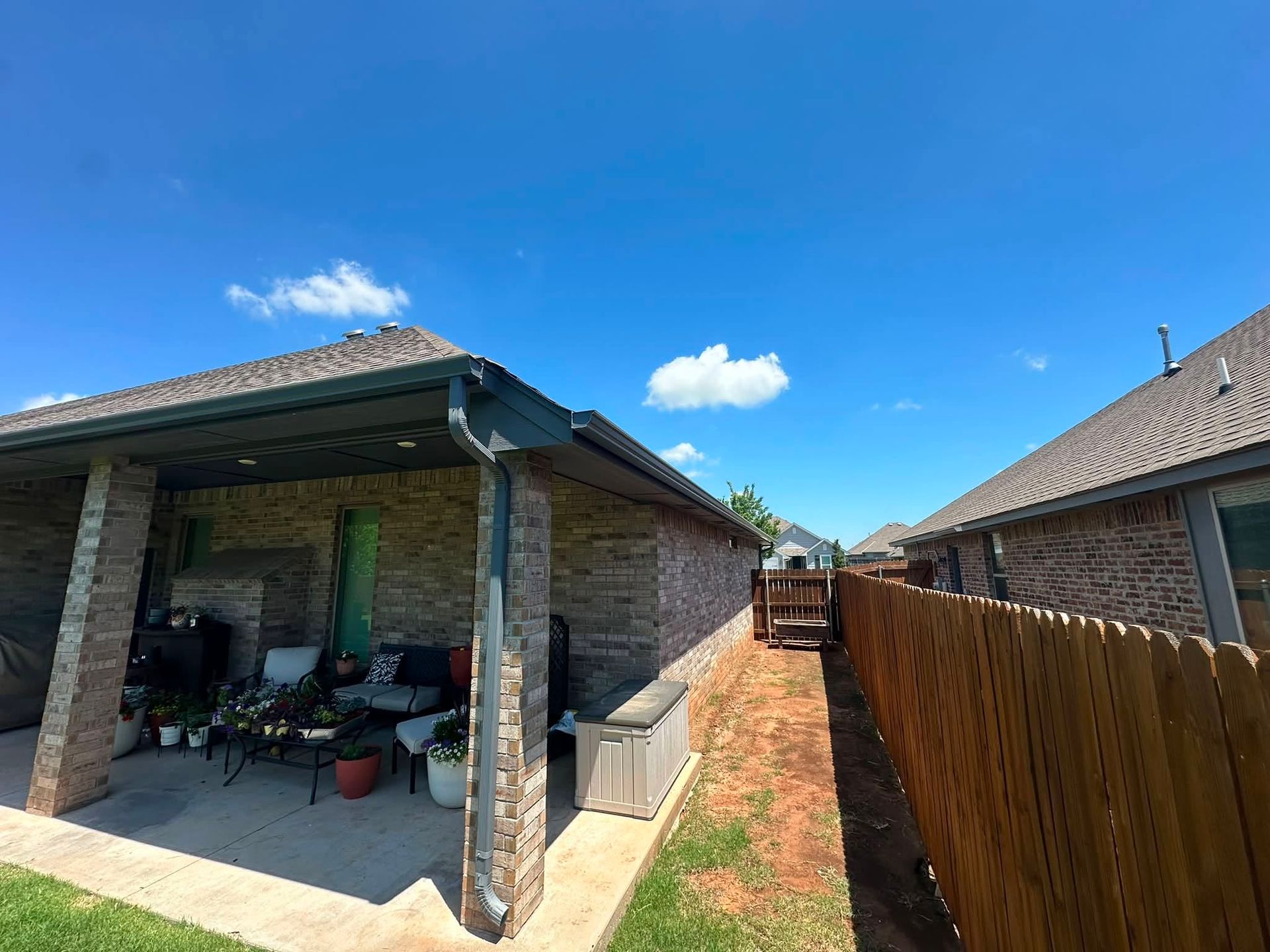 Backyard between two brick houses, with a covered patio and wooden fence under a blue sky