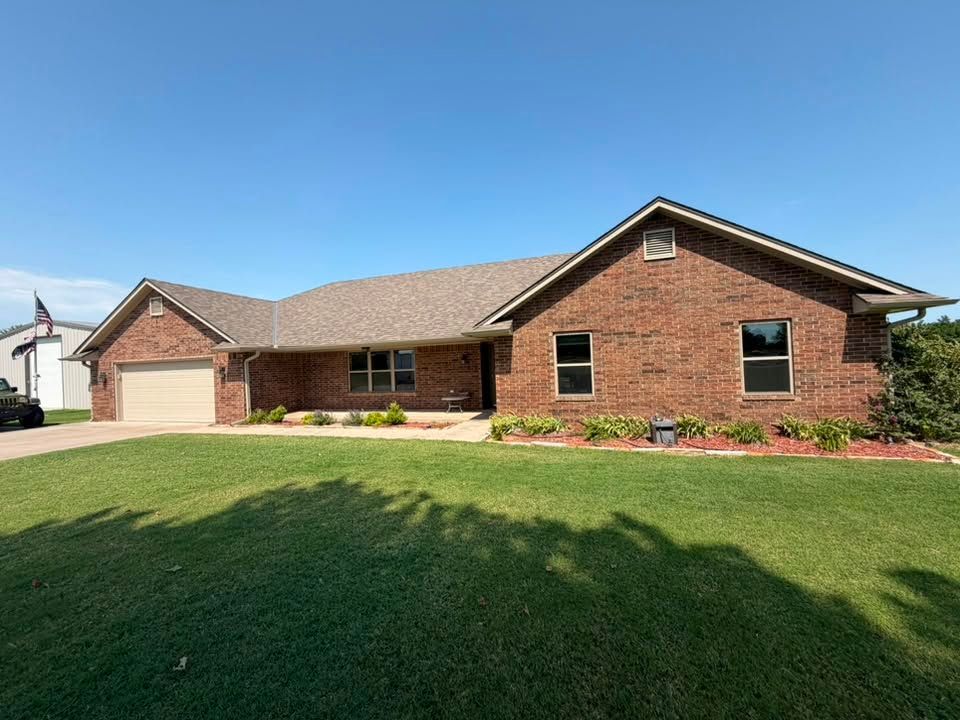 Single-story brick house with a two-car garage and large green lawn under a clear blue sky