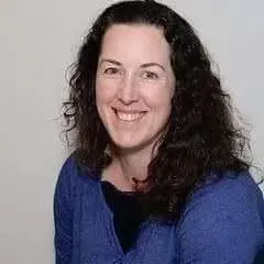 Woman with curly dark hair smiles, wearing a blue shirt against a white background.