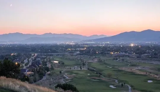Dusk over a golf course and city with mountains in the distance, light pink and orange sky.