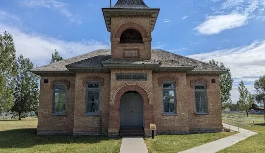 Brick schoolhouse with a bell tower, on a grassy lawn under a blue sky.