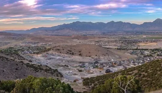 Scenic overview of a valley with mountains in the distance under a colorful sky.