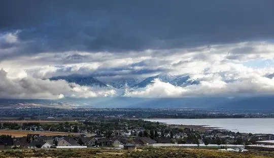 Overcast sky over lake and distant mountains with scattered residential buildings.