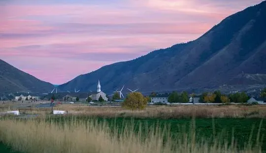 Sunset over a valley with a church steeple, mountains, and fields of tall grass.